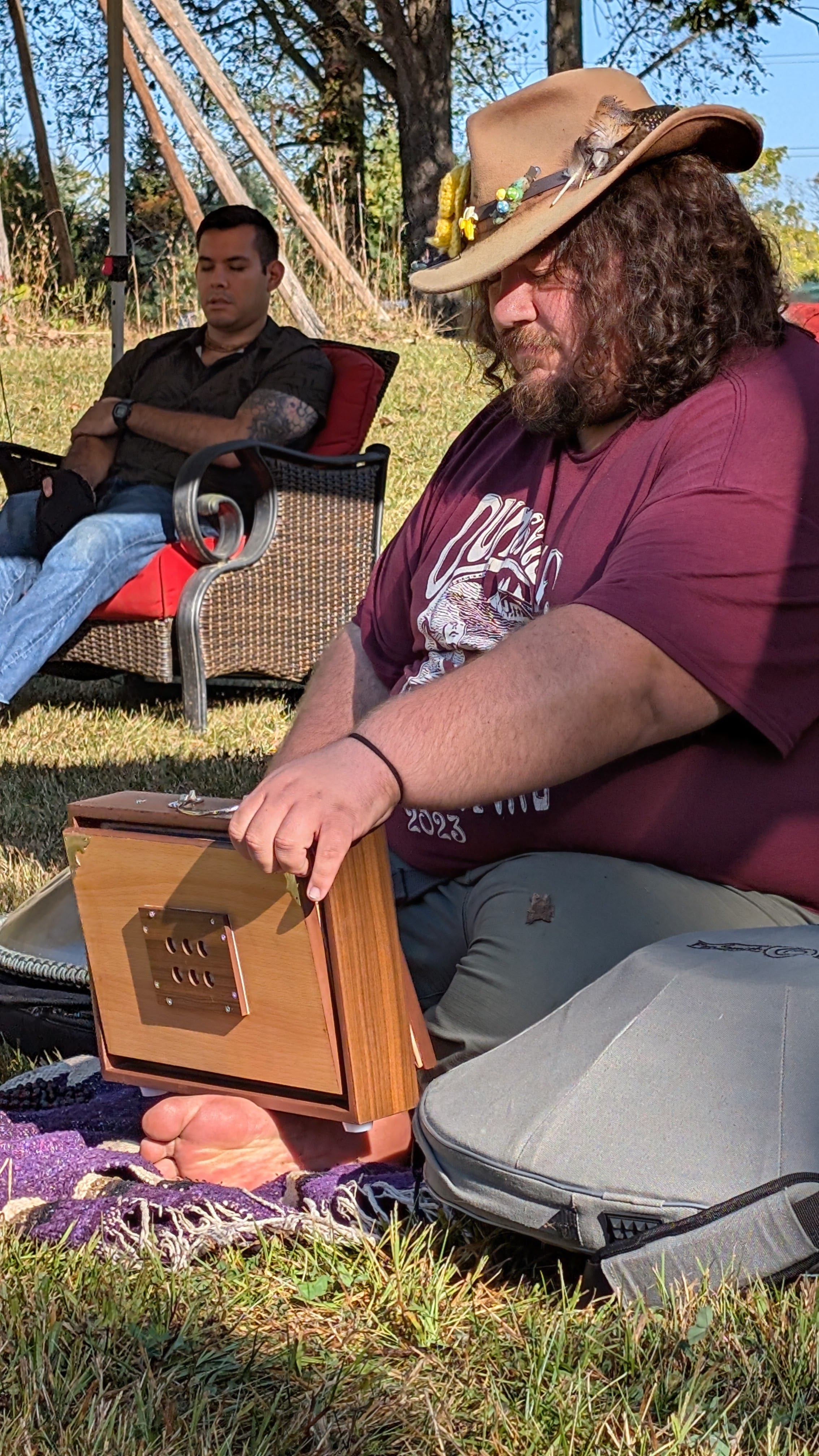 A musician seated outdoors with a wooden instrument during the gathering